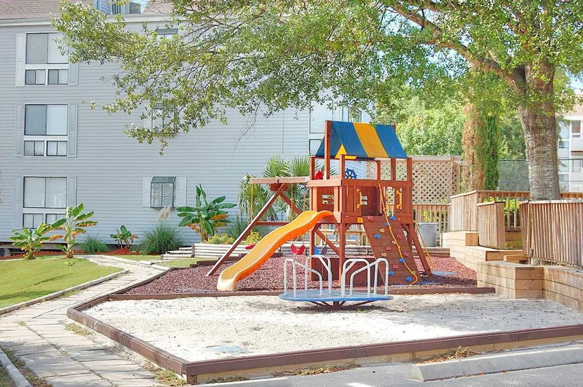 A vibrant playground with a slide and merry-go-round surrounded by lush landscaping. The scene is joyful and energetic, capturing children playing and families gathering nearby, suggesting ample opportunities for multi-generational fun and outdoor activities.