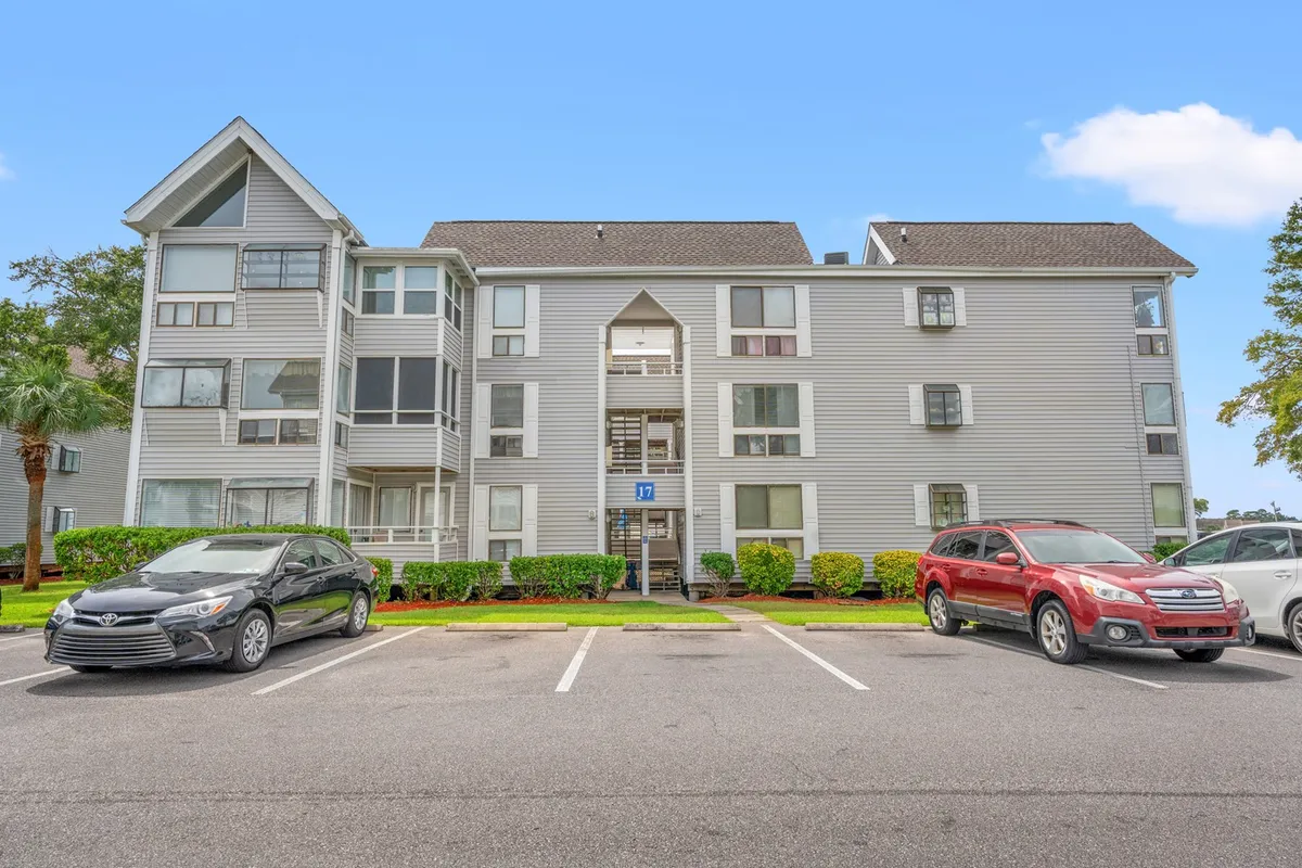 A wide-angle view of the Arcadian Dunes apartment complex, featuring well-kept landscaping, visible balconies, and a parking area. The scene is lively yet serene, giving a sense of a well-established community with spaces for both private relaxation and group socialization.