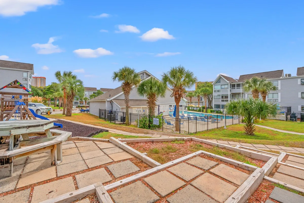 A family-friendly pool area adjacent to a playground, with palm trees and residential buildings in the background. Children play, families lounge, and the community atmosphere is evident, showcasing spaces ideal for relaxation and group fun.