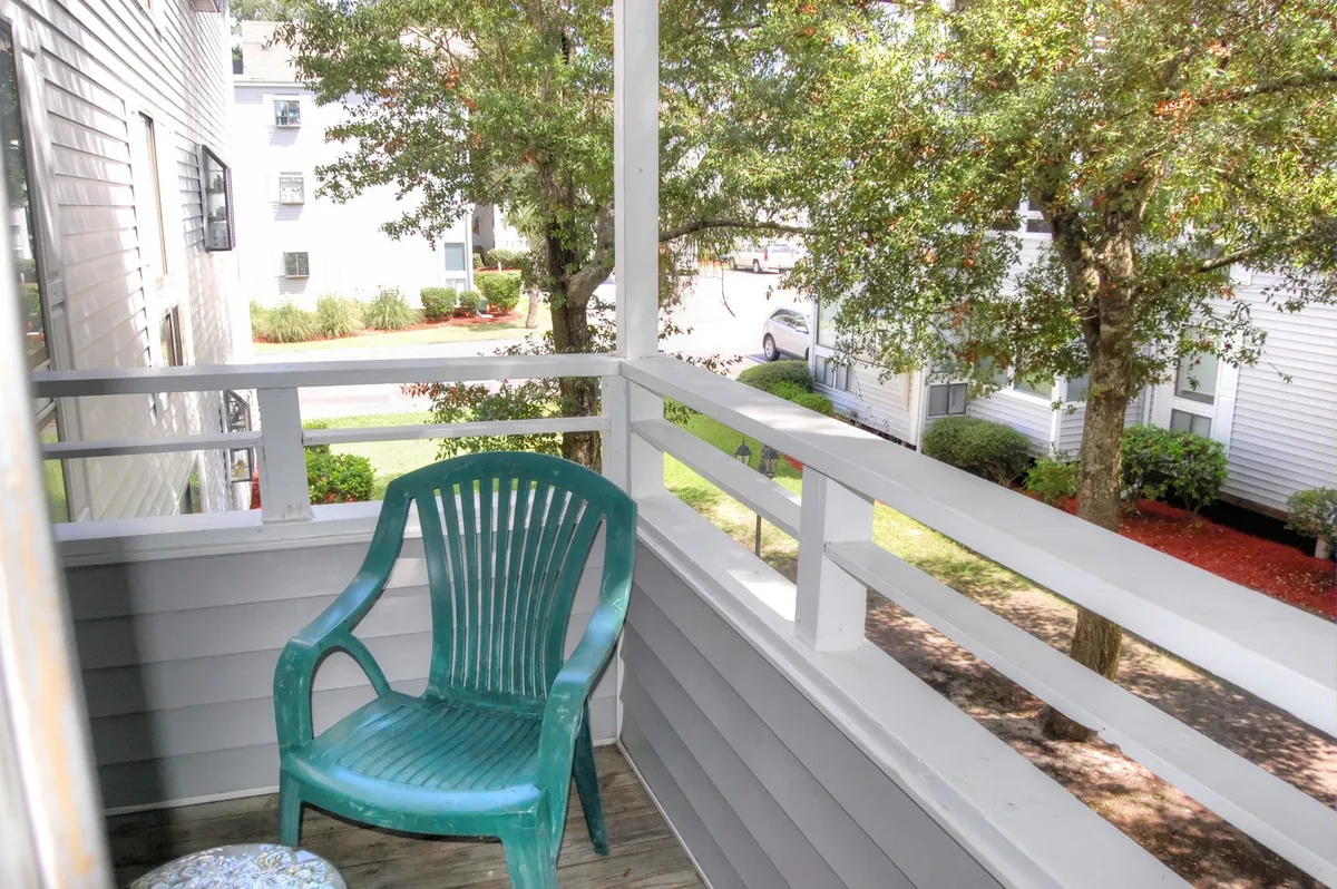 A tranquil wooden deck featuring a green plastic chair, surrounded by lush trees and overlooking a quiet pathway. The scene gives a sense of privacy and invites quiet moments for sipping coffee or enjoying the fresh air, likely from a balcony or patio connected to the property.