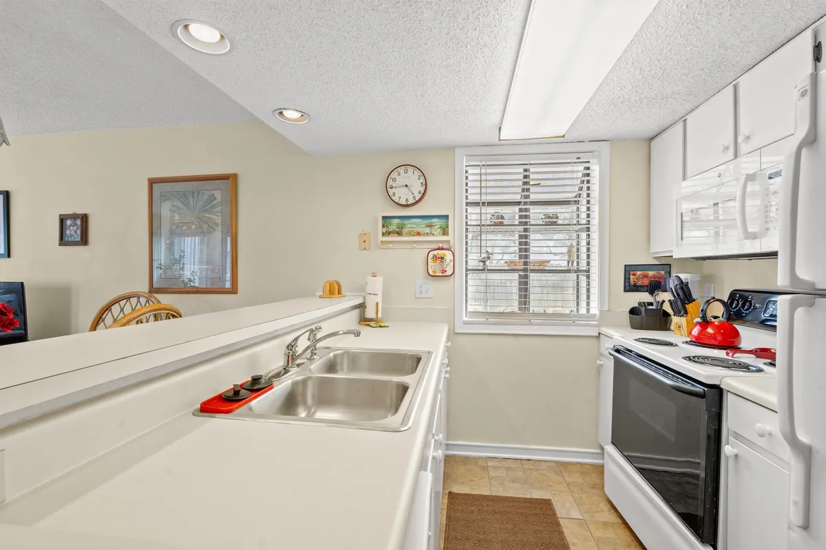 A welcoming kitchen interior featuring a prominent kitchen sink, a red kettle on the stove, modern appliances, and a wall clock. The arrangement suggests a space that is both functional and inviting, with countertops clear and ready for meal prep or casual gatherings.